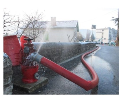 Poteau d'incendie rouge avec tuyau raccordé en fonctionnement, projetant de l'eau sous pression