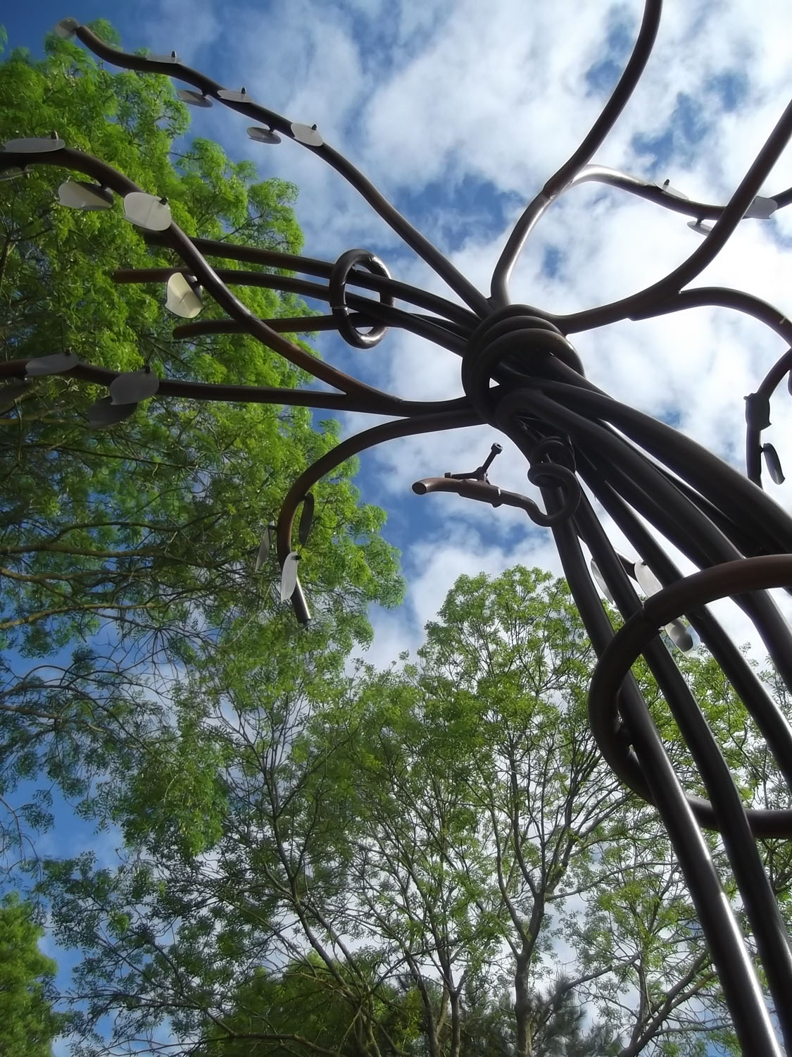 Sculpture métallique en forme d'arbre vue en contre-plongée, avec plaques commémoratives suspendues aux branches