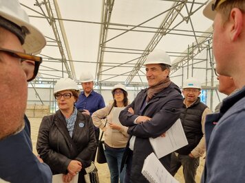 Élus et techniciens équipés de casques blancs échangent sous l'échafaudage couvert de la terrasse en restauration.