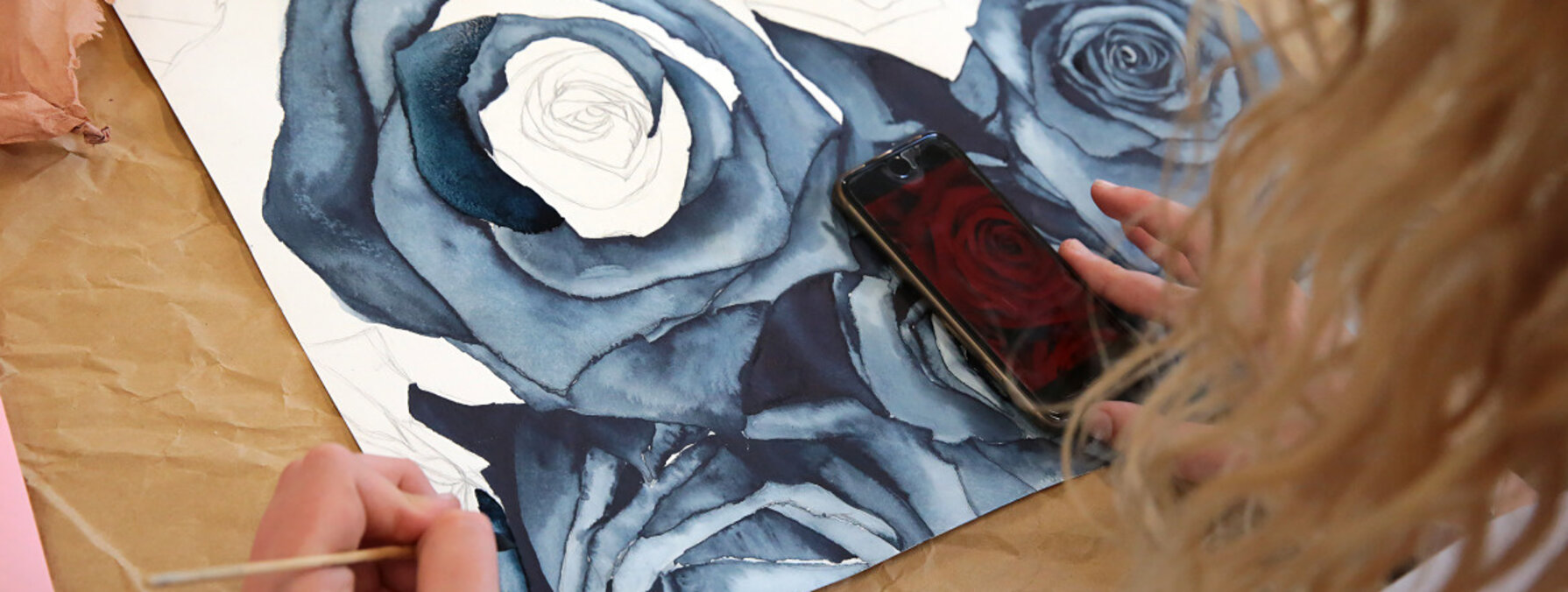 Élève réalisant une aquarelle de roses aux teintes bleues et grises, smartphone posé sur l'œuvre comme référence