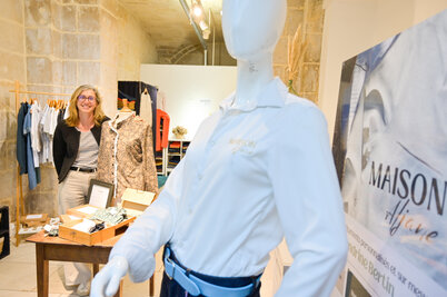 Sandrine Bertin souriante dans la boutique éphémère, avec un mannequin portant une chemise Maison Aljane au premier plan