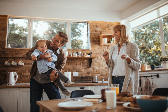 Parents et jeune enfant partageant un moment de joie dans une cuisine lumineuse au décor chaleureux.