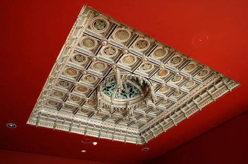 Plafond à caissons sculpté orné de médaillons dorés à rosettes et d'un lustre central, aux murs peints en rouge
