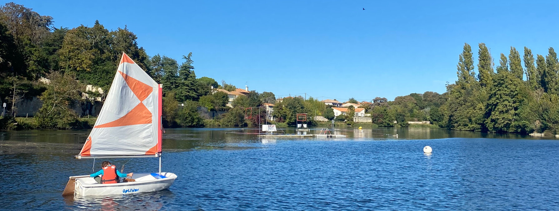 Enfant équipé d'un gilet de sauvetage pilotant un voilier Optimist sur le plan d'eau par beau temps