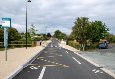 Voie cyclable aménagée avec marquage au sol jaune et blanc, séparée de la chaussée, longeant un arrêt de bus ligne 23