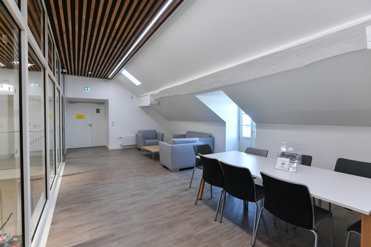 Novembre 2019 Salle commune avec table et chaises noires, canapés gris et cloison vitrée sous poutre de charpente apparente