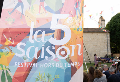 Affiche « Festival hors du temps » au premier plan, public nombreux assistant à un spectacle de plein air dans un cadre villageois