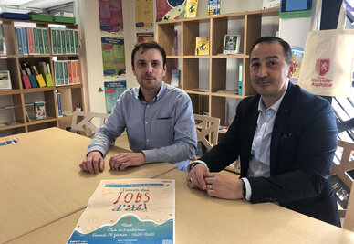 Deux représentants posent dans les locaux d'Info Jeunes Niort avec l'affiche du Forum des jobs d'été sur la table.