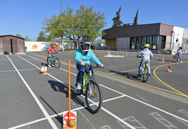 Enfants casqués manœuvrant à vélo sur un parcours balisé de cônes et marquages au sol dans une cour d'école