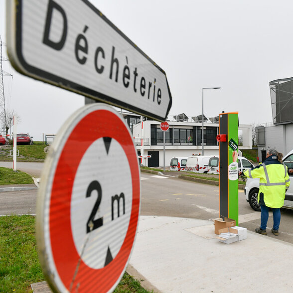 Technicien en gilet fluorescent opérant une borne d'accès verte à l'entrée du centre, un véhicule en attente - Agrandir l'image, fenêtre modale