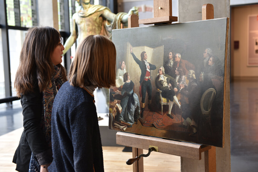 Deux visiteurs contemplant le tableau restauré posé sur un chevalet dans une salle d'exposition