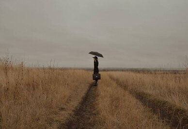Concours de nouvelles des médiathèques une femme dans un champ. Elle s'abrite sous un parapluie et tient une sacoche à la main.