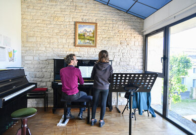Cours de piano à l'antenne de Chauray : un professeur au clavier accompagne un élève debout face à la partition