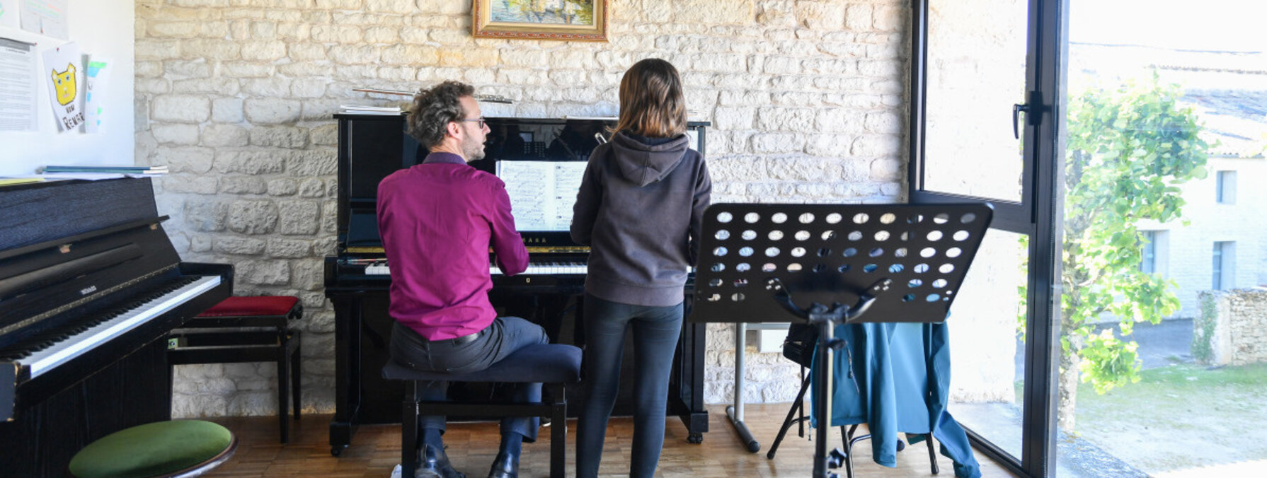 Cours de piano à l'antenne de Chauray : un professeur au clavier accompagne un élève debout face à la partition