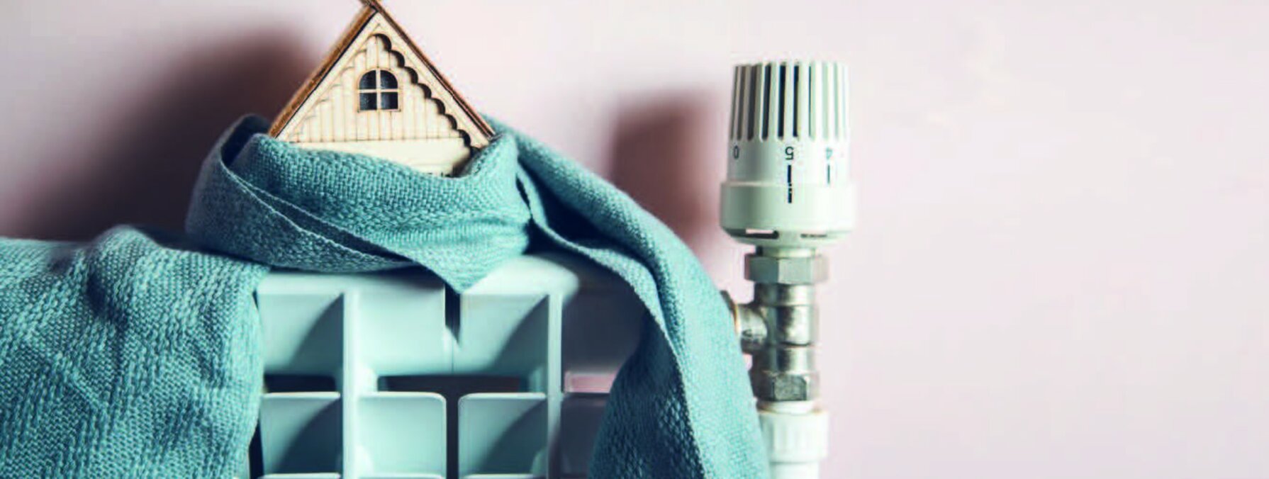 Maquette de maison enveloppée dans un tissu posée sur un radiateur avec tête thermostatique