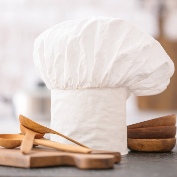 Toque blanche de cuisinier entourée d'ustensiles et bols en bois posés sur un plan de travail de cuisine - Agrandir l'image, fenêtre modale