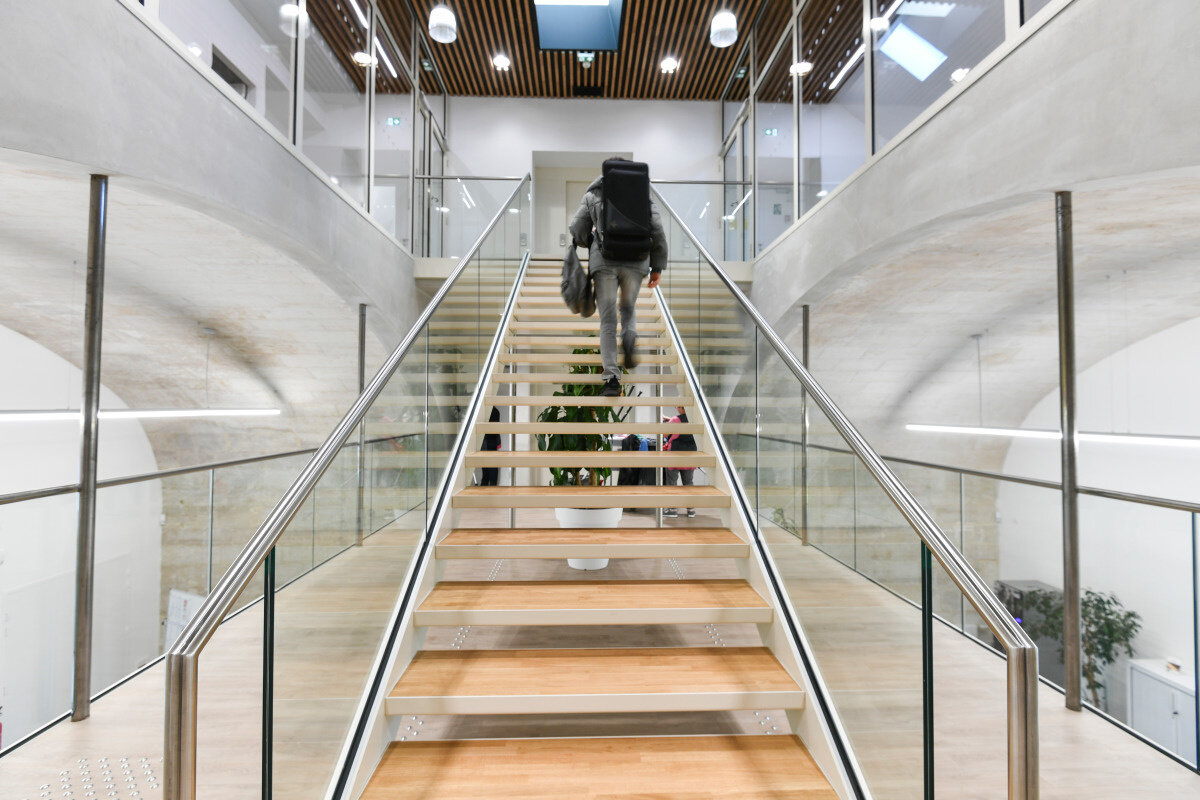 Novembre 2019 Hall du Conservatoire, escalier central à rampes vitrées, un élève portant un étui d'instrument monte les marches