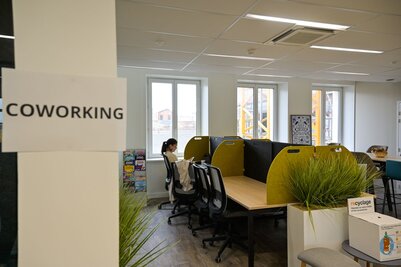 Salle de coworking réaménagée avec postes de travail équipés de cloisons acoustiques, grue de chantier visible par les fenêtres