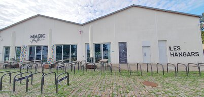 Les Hangars, bâtiment blanc avec enseigne Magic Flon Flon, arceaux vélos et tables de pique-nique au premier plan
