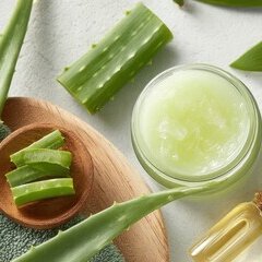 Feuilles d'aloe vera tranchées, bocal de gel vert et flacons d'huile à bouchon liège sur fond blanc
