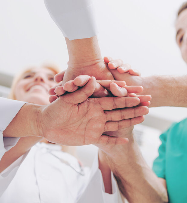 Équipe soignante en blouse et tenue médicale unissant leurs mains en cercle, illustrant la coopération professionnelle