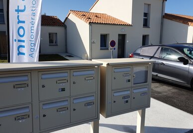 Boîtes aux lettres collectives devant des maisons individuelles neuves, avec la bannière Niort Agglomération