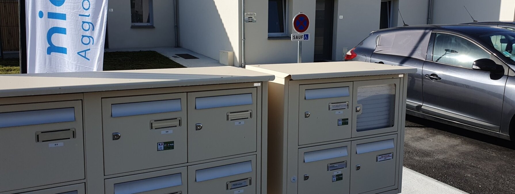 Boîtes aux lettres collectives devant des maisons individuelles neuves, avec la bannière Niort Agglomération