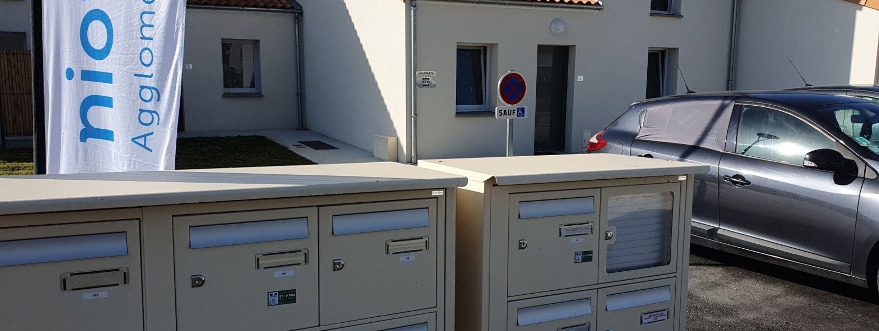 Boîtes aux lettres collectives devant des maisons individuelles neuves, avec la bannière Niort Agglomération