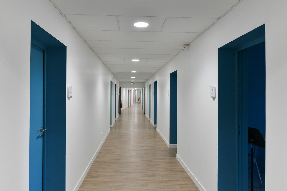 Novembre 2019 Couloir du Conservatoire avec portes bleues, murs blancs et parquet clair, un pupitre de musique visible dans une salle